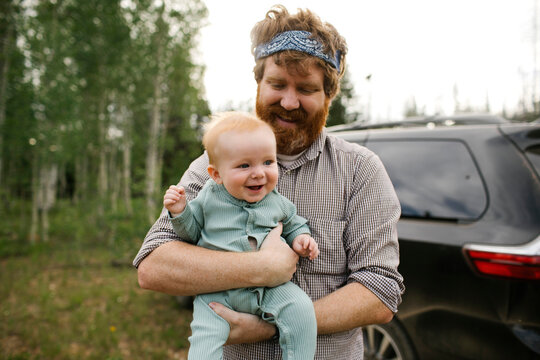 USA, Utah, Uinta National Park, Smiling man holding baby son (6-11 months) in field, car in background