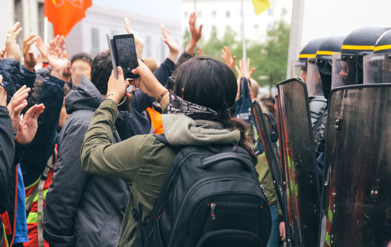 jeune femme en train de photographier des policiers avec son téléphone lors d'une manifestation