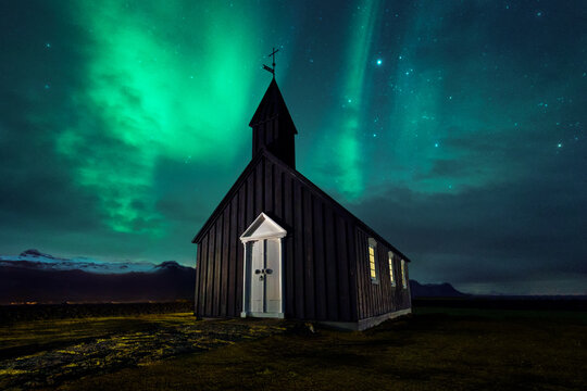 Magnificent scenery of wooden church located on meadow on background of sky with aurora borealis phenomenon in Iceland at night