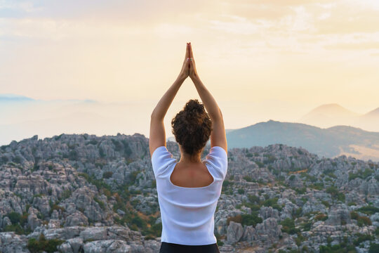 Full body back view of unrecognizable barefoot female standing in Star pose with reverse prayer hands on top of mountain while practicing yoga in nature at sunset time