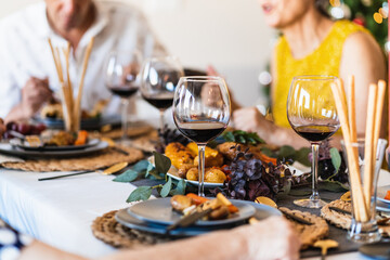 Dining table served with glasses and plates against blurred glowing Christmas tree on Christmas eve at home