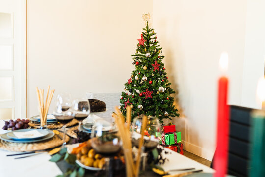 Festive table setting near decorated Christmas tree with glowing garlands before Christmas celebration party