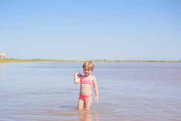 Fototapeta premium Portrait of a cute little girl in pink swimming suit on beach