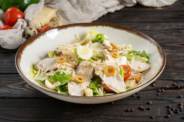 Caesar salad with chicken fillet. Lettuce, olives, cheese, cherry tomatoes, quail egg, and crunchy croutons in a ceramic plate on a wooden kitchen table. Cold appetizer.