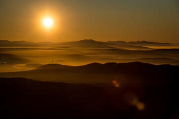 the sun sets below the horizon and illuminates the fog in the valley with a yellow light