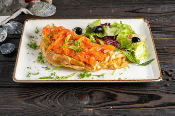 Omelet with salmon and mix salad. A classic hot breakfast dish with eggs, milk, salmon or trout and various types of fresh green salad with olives, olives and cherry tomatoes.
