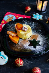 New Year's food for children from cereal porridge and pieces of baked pumpkin. A festive setting of a flashlight, Christmas balls and beautiful food decoration on a plate and on a black background.