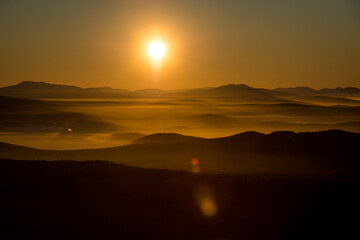 the sun sets below the horizon and illuminates the fog in the valley with a yellow light
