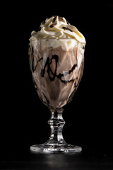 Chocolate milkshake with chocolate and cream in a glass on a black background. Protein sweet cocktail with chocolate. Cold drink.