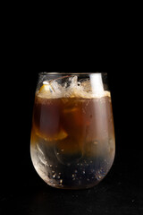 Espresso tonic. Cold alcoholic cocktail of coffee and a refreshing tonic in a transparent glass on a black background.