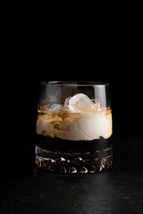 Cocktail White Russian. Cold alcoholic cocktail of cream, coffee liqueur, vodka and ice in a transparent glass on a black background.