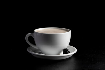 White coffee mug with raf coffee and blackberries on a saucer on a black background.