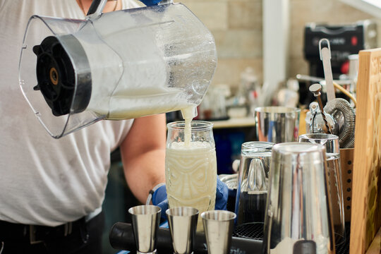 Cropped unrecognizable informal male bartender pouring milkshake in glass at counter