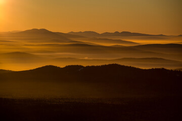 the sun sets below the horizon and illuminates the fog in the valley with a yellow light