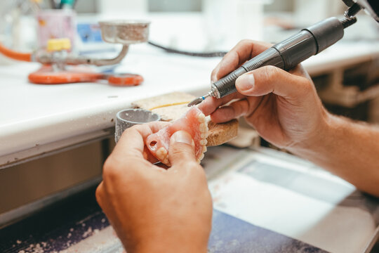 Unrecognizable male technician working in lab and using polishing machine for producing denture