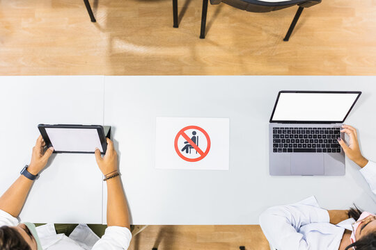 Top view of anonymous female coworkers using netbook and tablet with black screens while sitting at desk with prohibit sign