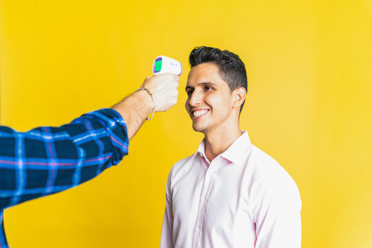 Crop unrecognizable male measuring temperature of happy colleague using digital thermometer on yellow background