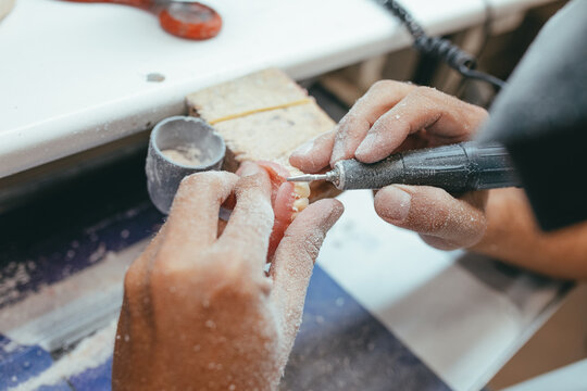 Unrecognizable male technician working in lab and using polishing machine for producing denture