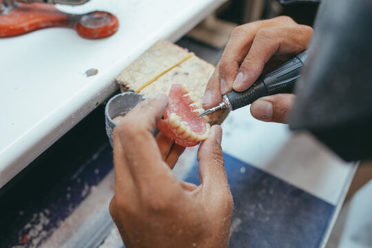 Unrecognizable male technician working in lab and using polishing machine for producing denture