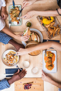 Top view crop multiethnic friends gathering at table in modern restaurant and having tasty dinner including meat balls spring rolls and sandwiches