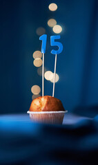 Birthday cake or muffin with fifteen (15) number and lights on the blue background. Birthday or...