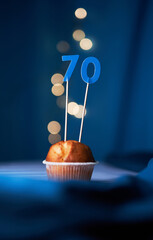 Birthday cake or muffin with seventy (70) number and lights on the blue background. Birthday or...