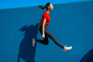 Happy woman in red dress jumping on a blue background. Woman jumping and having fun. Happiness and joy concept.