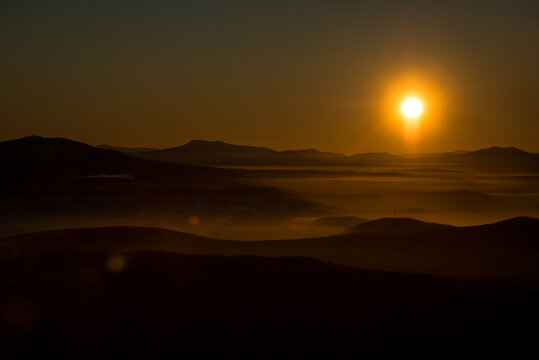 the sun sets below the horizon and illuminates the fog in the valley with a yellow light