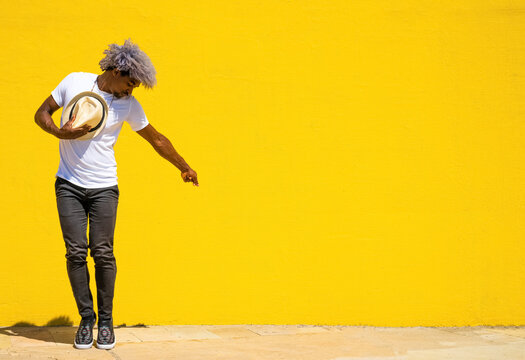 Black man with afro hair and hat dancing on a yellow background. Dancing with a hat.