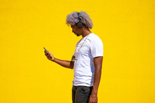 Black man with afro hair listening to music with earphones on a yellow background. Listening to music.