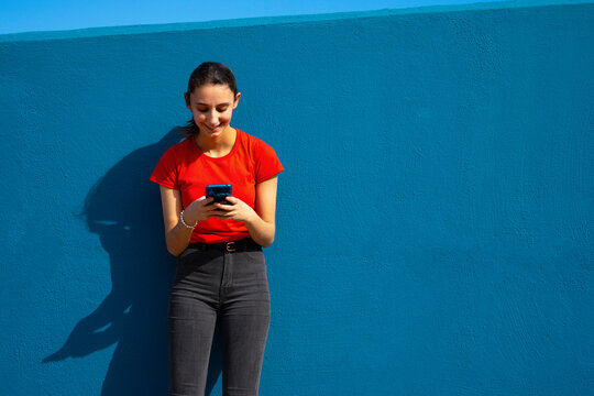 Woman dressed in red using the mobile on a blue background. Concept of using the mobile. Blue background.