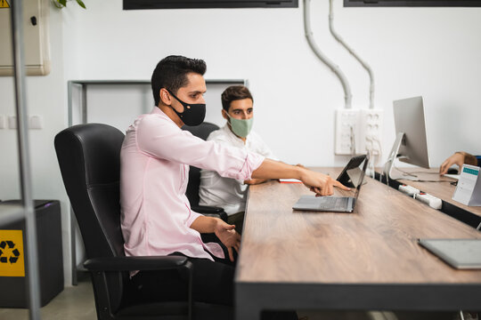 Side view of anonymous entrepreneurs in formal apparel and face masks working on project while surfing internet on netbook at office table