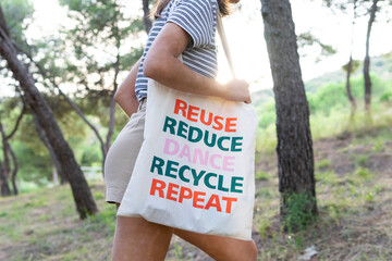 Side view of unrecognizable female walking in woods with reusable eco friendly bag while showing zero waste concept