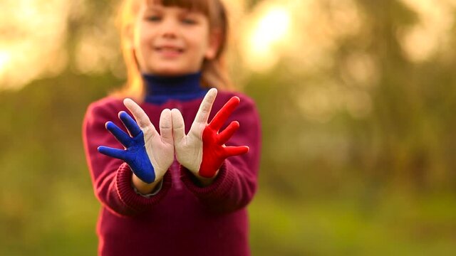 Freedom France concept. Cute child forming flying bird gesture with painted in France colors hands at bright sunset background.