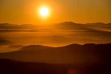 the sun sets below the horizon and illuminates the fog in the valley with a yellow light