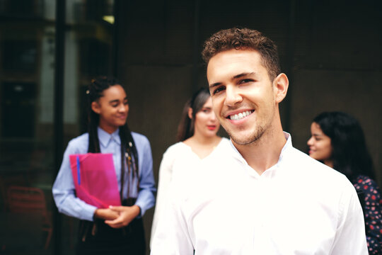 Young smiling man looking at camera behind multiracial coworkers