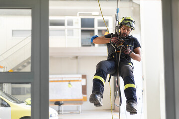 Young fireman in protective hardhat and gloves ascending wall on colorful rope during routine practices