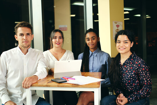 Cheerful multiethnic colleagues looking at camera while they are sitting at table with netbook in building