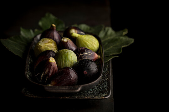 From above of fresh sweet figs arranged on green leaves on black table