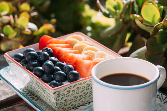 Appetizing breakfast with various fruits and berries arranged on wooden table with cup of aromatic coffee in outdoors cafe