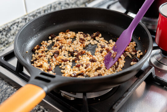 Frying pan with raisin and pine nuts for Catalan cod dish placed on stove during cooking preparation in home kitchen