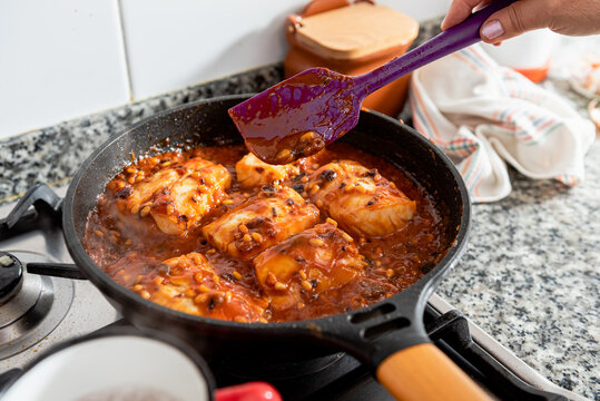 Closeup of frying pan with cod steaks and aromatic spicy red sauce with raisin and pine nuts placed on stove during preparation of typical Catalan dish