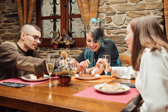 Front View Of Group Of Hipsters Sitting Together At Table In Restaurant And Sharing Dessert