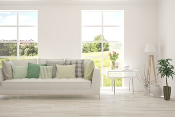Fototapeta premium White living room with sofa and summer landscape in window. Scandinavian interior design. 3D illustration