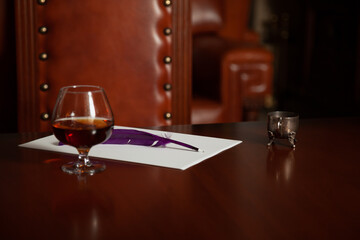 Glass of cognac and inkwell on polished table