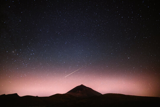 Spectacular scenery of glowing starry night sky with falling star over dark mountain range