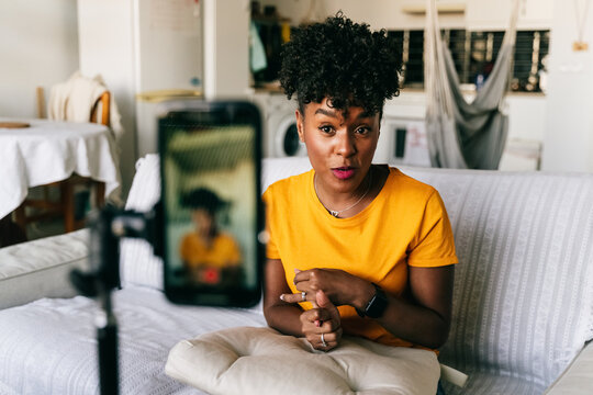 Cheerful young African American female blogger recording video on smartphone while preparing content for social networks at home