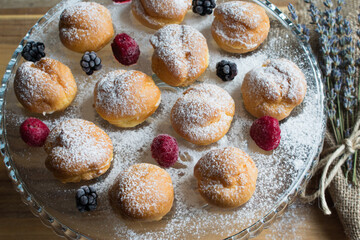 Presentation of raspberry and blackberry and profiteroles. Delicious profiteroles with vanilla cream and powdered sugar.