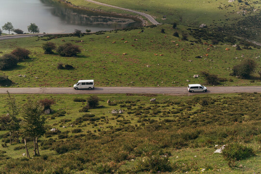 From above picturesque scenery of cars driving along narrow rural road running through lush verdant valley near tranquil lake