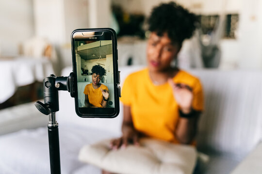 Cheerful young African American female blogger recording video on smartphone while preparing content for social networks at home